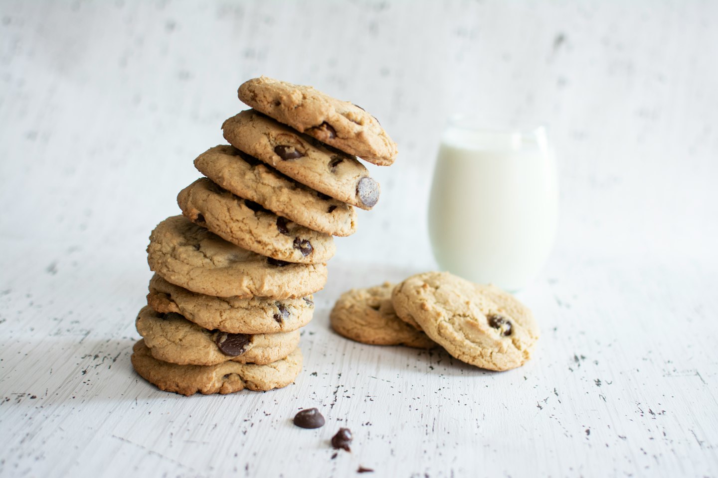 Stack of freshly baked chocolate chip cookies next to milk.