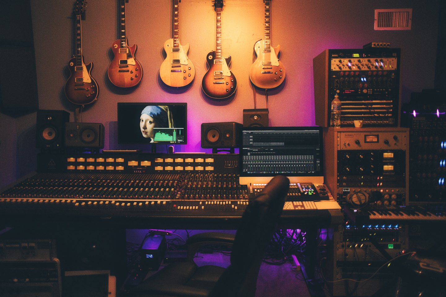 Mixing console and guitars in a purple-lit recording studio.